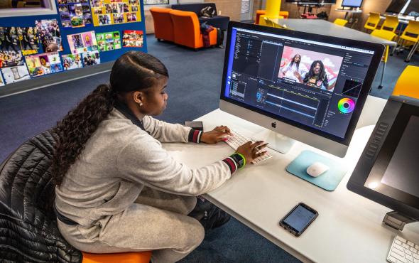 Young, black woman sitting at a desk editing a video