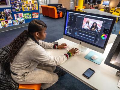 Young, black woman sitting at a desk editing a video